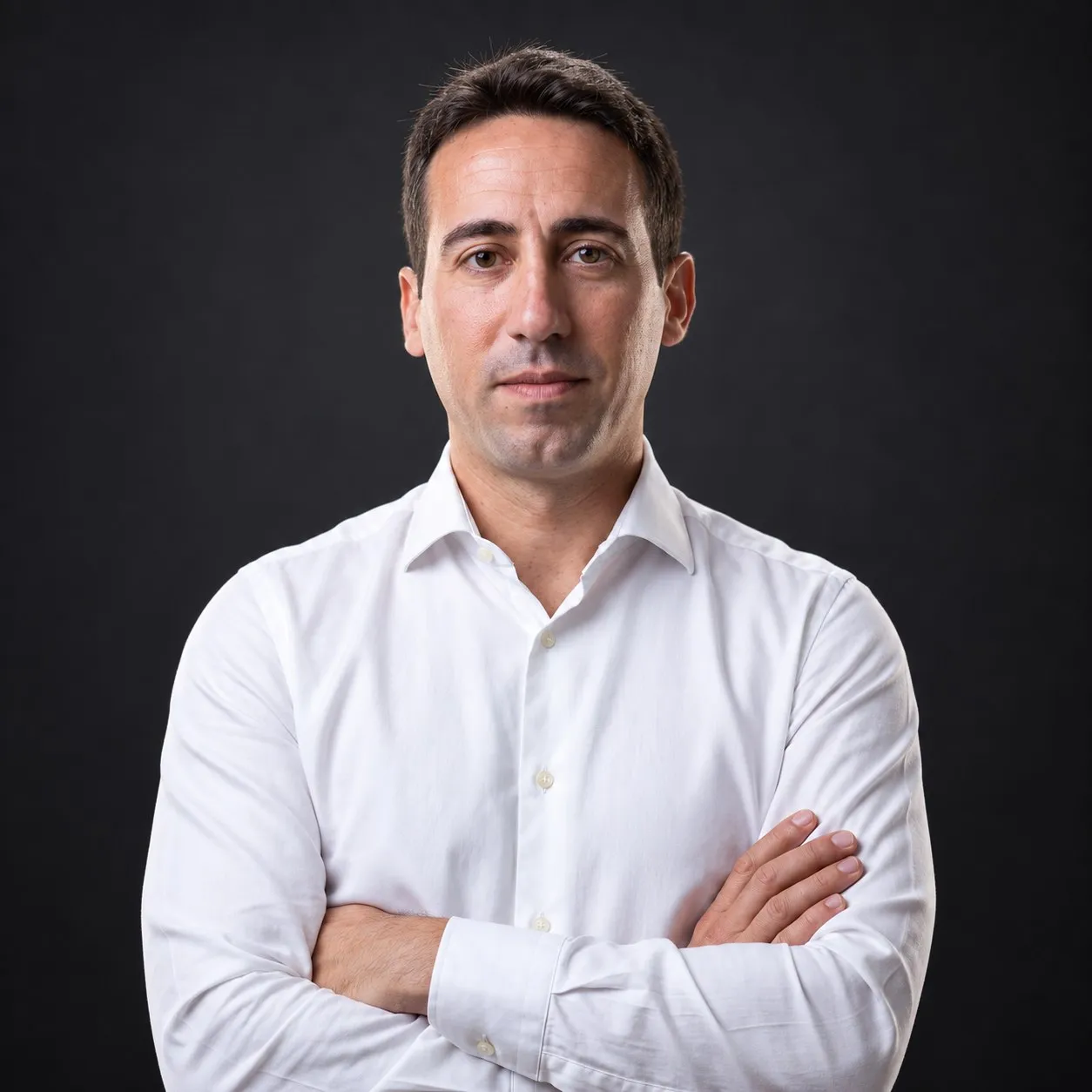 Retrato de estudio de Manuel Liria, con camisa blanca y los brazos cruzados, sobre fondo gris oscuro